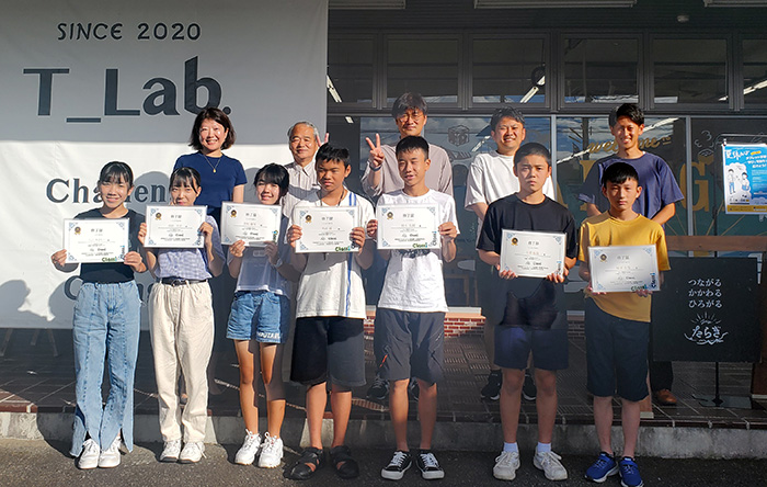 修了証を掲げた子供たちが前列に、大人が後列に並んで写真撮影